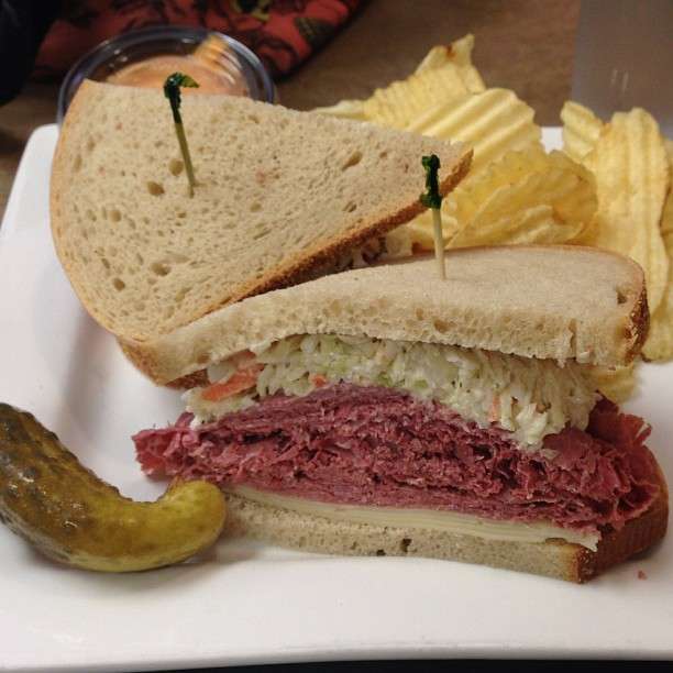 A corned beef sandwich with coleslaw and pickles on a white plate.